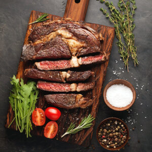 Grilled ribeye beef steak with red wine, herbs and spices on a dark stone background.