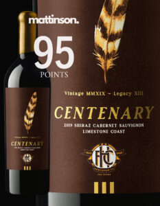 Close-up of a wine bottle labeled 'Centenary 2019 Shiraz Cabernet Sauvignon Limestone Coast.' The label is dark brown with gold text, featuring an illustrated brown-and-gold feather above the word 'Centenary' and the Hawthorn Football Club centenary logo (1925–2025) at the bottom. The bottle has a gold wax-dipped capsule and the design includes both a full bottle view and a zoomed-in section of the label. Also featured is a Campbell Mattinson logo that features their 95-point rating of this wine.