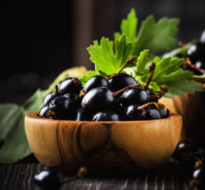 Fresh black currants in wooden bowls, on black kitchen table background, copy space, selective focus